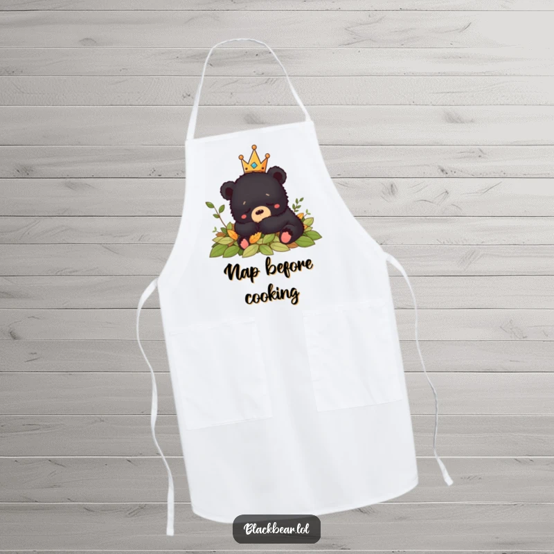 Funny black bear cub wearing a crown naps peacefully in leaves while cooking on this humorous apron.