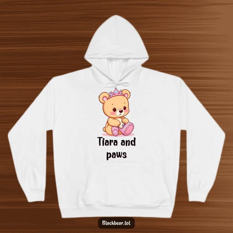 Funny Hoodie: Adorable bear cub wearing a sparkly tiara, curiously trying on giant, shimmering shoes.