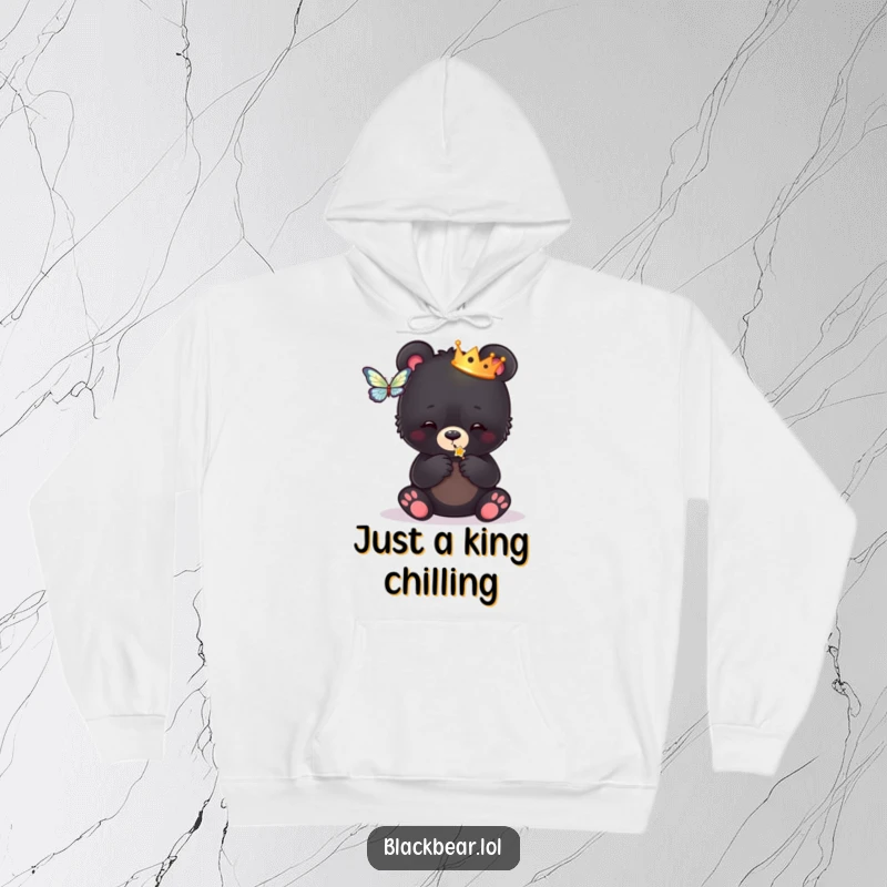 Funny hoodie print of a black bear cub wearing a tiny crown, playfully swatting at a butterfly, radiating regal amusement.