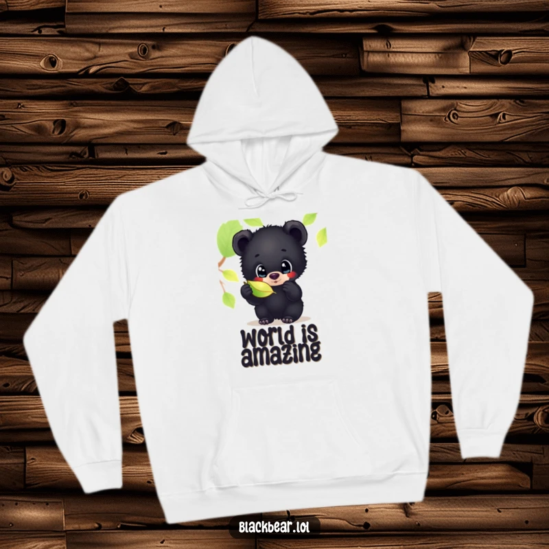 Funny hoodie featuring a black bear cub with wide, curious eyes, mesmerized by the delicate shimmer of a fallen leaf, evoking wonder.