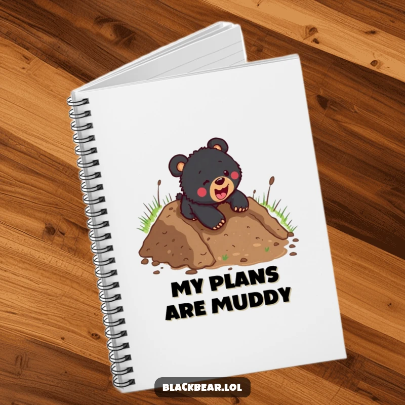 Funny black bear cub sliding headfirst down a muddy hill, on the cover of a notebook, inspiring messy creativity and fun.