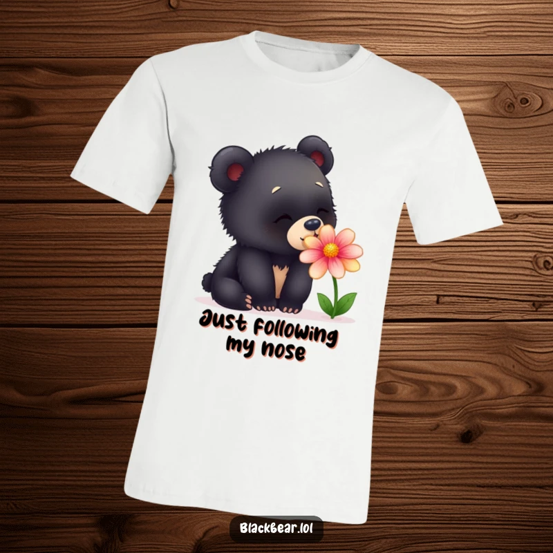 Funny t-shirt showcasing a young black bear cub curiously sniffing a brightly colored flower, looking utterly charmed and happy.