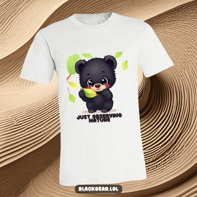 Funny t-shirt depicting a black bear cub with large, curious eyes, captivated by the shimmering beauty of a single, detailed leaf.