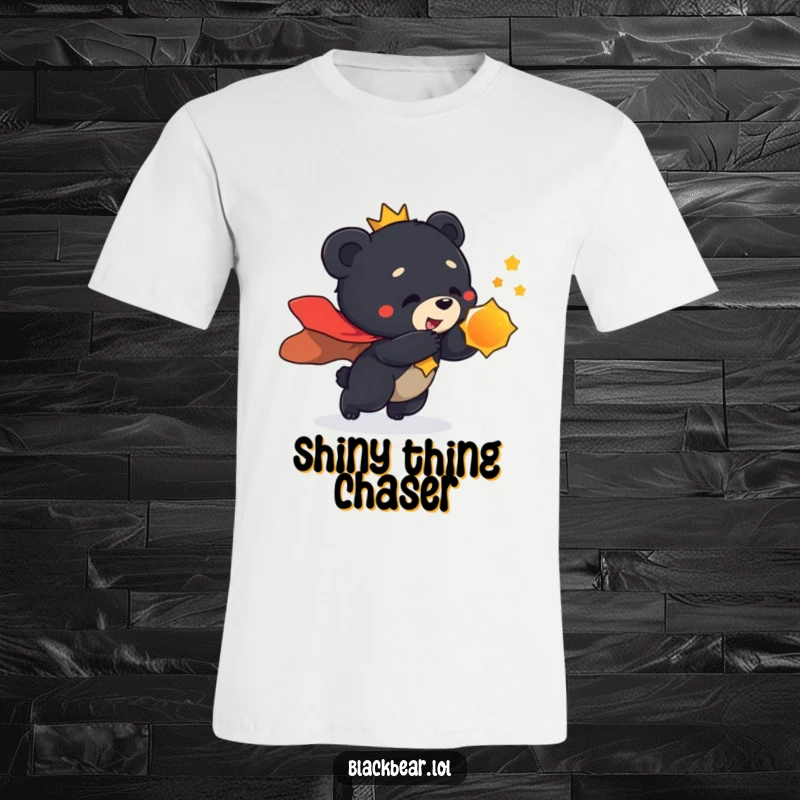 Funny t-shirt graphic of a black bear cub in a grand cape, playfully pouncing towards a dazzling, shiny object.