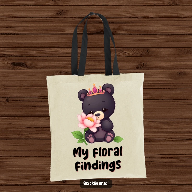 Funny tote bag with a black bear cub wearing a tiara, sniffing a giant flower, ready for nature outings.